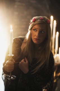 Sorceress holding candle in dark room.