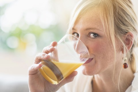 Woman sitting in living room and drinking orange juice.