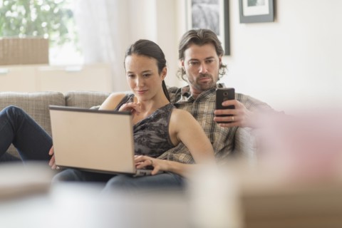 Couple on sofa, woman using laptop and man mobile phone.