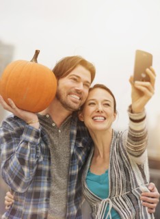 Couple taking selfie with mobile phone, man holding pumpkin.