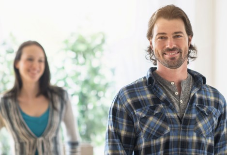 Smiling man looking at camera, woman in background.