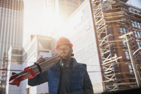 Construction worker carrying tripod on shoulder.
