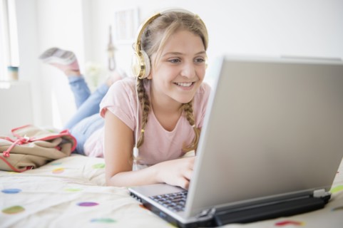 Girl (12-13) lying in bed using laptop