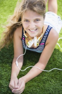 Girl (12-13) lying in grass with headphones