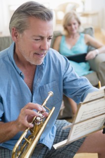 Portrait of senior man holding trumpet looking at music stand with woman on sofa in background