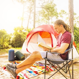 Man reading book in front of tent