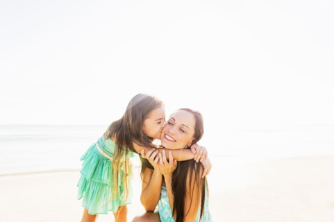 Girl (6-7) kissing her mother on cheek on beach