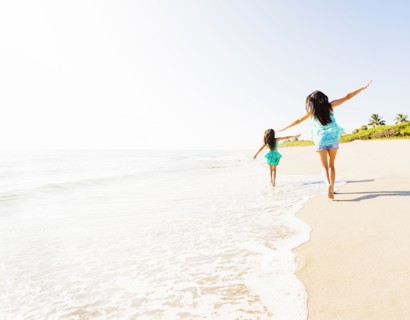 Rear view of girl (6-7) and her mom running on beach