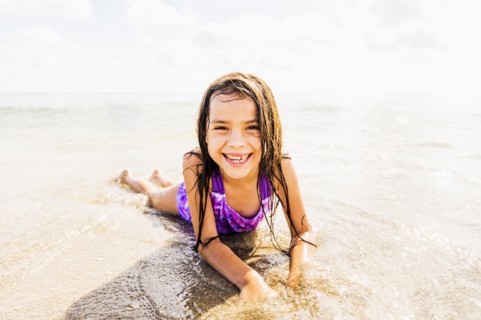 Portrait of girl (6-7) lying in sand on beach
