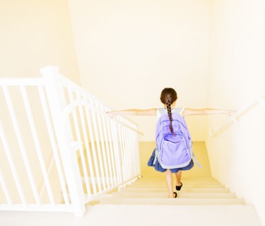 Girl (6-7) with backpack walking down stairs at home