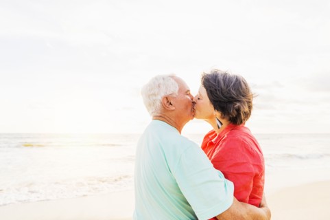 Older couple kissing on beach at sunrise