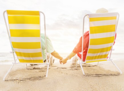 Rear view of couple sitting in lounge chairs on beach