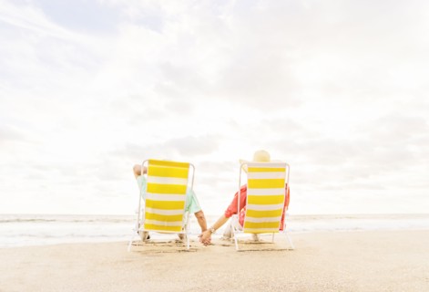 Rear view of couple sitting in lounge chairs on beach
