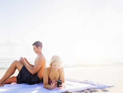 Portrait of young couple relaxing on beach, using smart phones