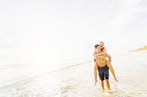 Boyfriend walking in surf carrying girlfriend piggyback