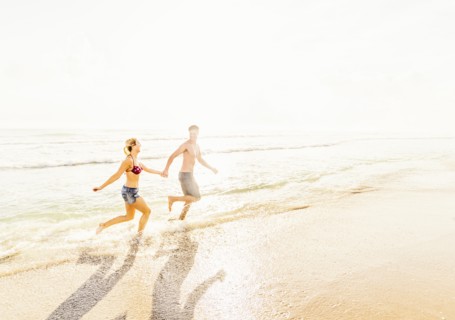 Young couple running in surf holding hands