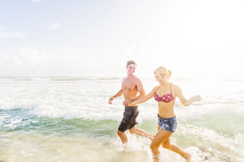 Young couple running in surf holding hands