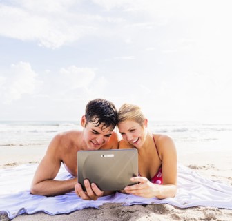 Portrait of young couple lying on blanket on beach side by side, using digital tablet