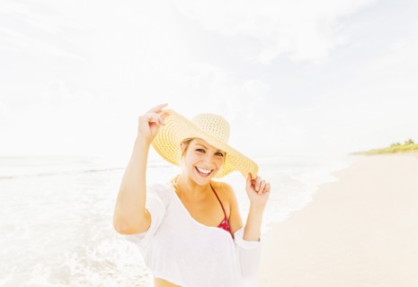 Portrait of smiling young woman on beach wearing sun hat