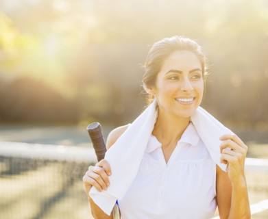 Portrait of smiling young woman with towel and tennis racket