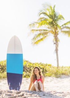 Portrait of young woman sitting near surfboard on beach