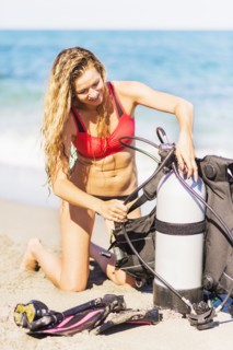 Young woman kneeling on sandy beach putting together scuba diving equipment