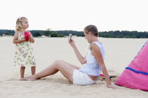 Mother taking picture of daughter (2-3) on beach