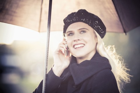 Smiling woman under umbrella using mobile phone