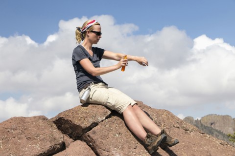 Woman sitting on rock and applying suntan lotion