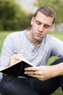 Portrait of young man writing journal in park