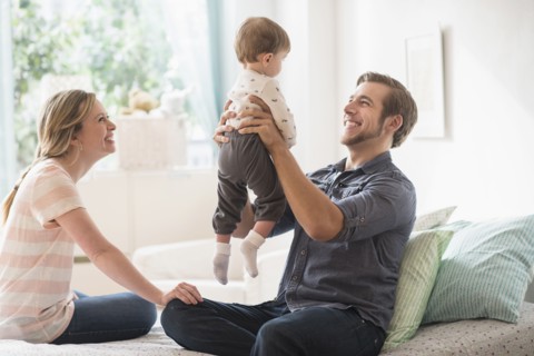 Happy parents playing with little son (2-3 years) on bed.