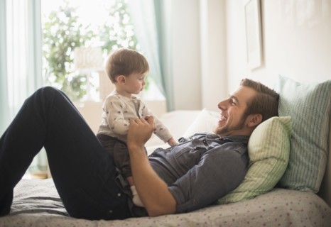 Happy father playing with little son (2-3 years) on bed.