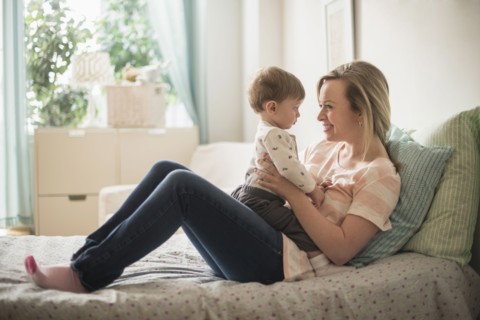 Happy mother playing with little son (2-3 years) on bed.