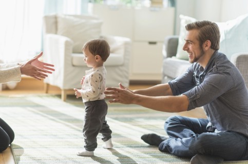 Happy parents helping little son (2-3 years) walking in living room.