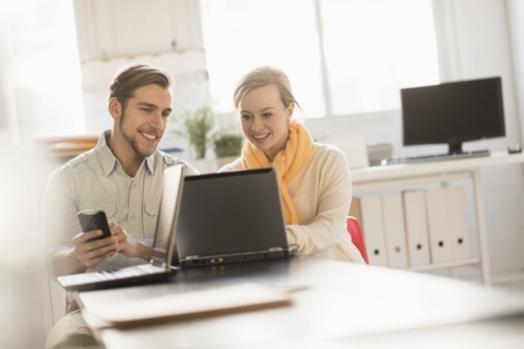 Young man and woman working together with laptop in office.