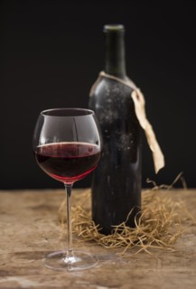 Still life with red wine glass and bottle on wooden table, studio shot.