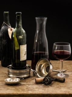 Still life with red wine glass, carafe and bottles on wooden table, studio shot.