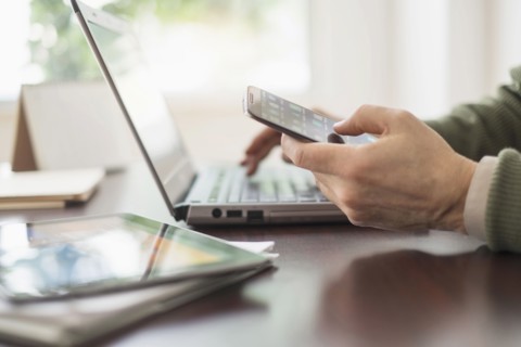 Close up of man's hands working at desk with electronic devices.