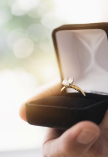 Close up of man's hand holding open box with engagement ring.