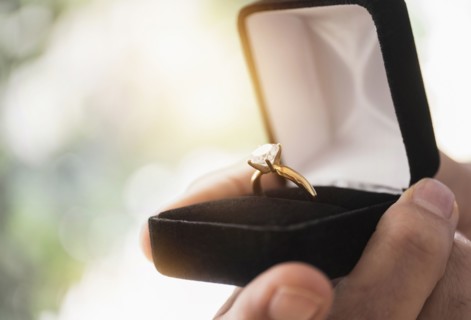 Close up of man's hand holding open box with engagement ring.
