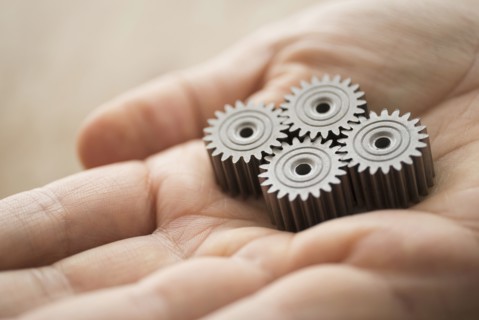 Close up of man's hand holding metal cogs.