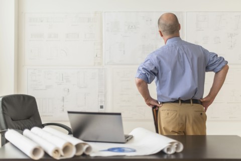 Mature architect looking at blueprints in office.