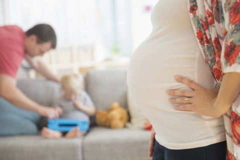 View of pregnant woman in living room, father and son (2-3) in background