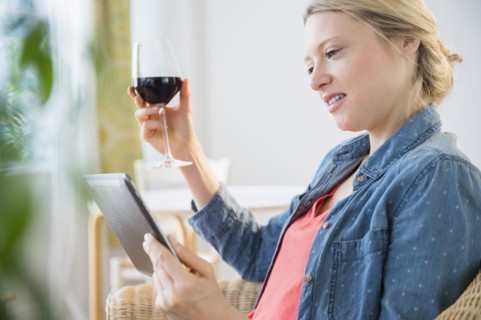 Woman sitting with digital tablet and glass of red wine