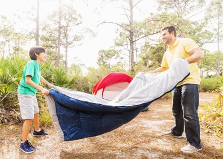 Father and son (12-13) preparing sleeping bag for camping