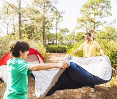 Father and son (12-13) preparing sleeping bag for camping