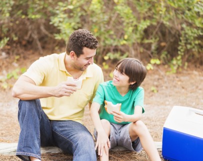 Father and son (12-13) eating sandwiches in forest
