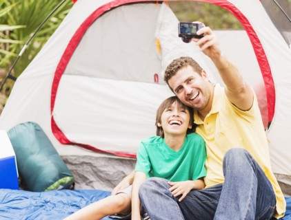 Father and son (12-13) taking selfie in front of tent