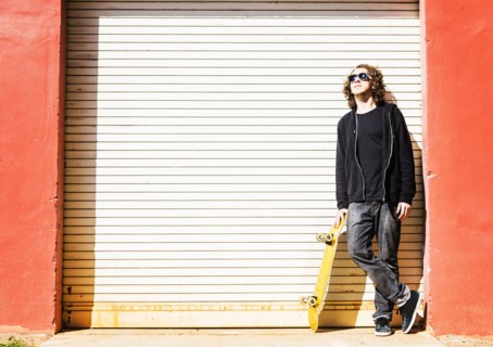 Man with skateboard leaning on garage door