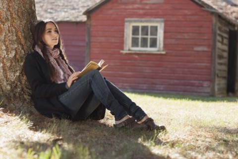 Woman with book sitting under tree